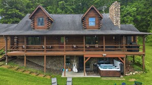 A log cabin with a balcony, a hot tub, and a stone chimney.