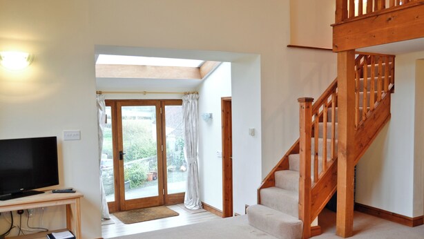 Un salon avec un téléviseur, un escalier en bois et une vue sur l’extérieur.