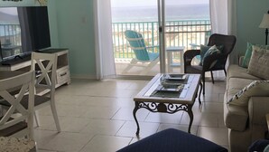 A living room with a TV, a dining table, a sofa, and a view of the beach. - Ocean View, Beach Front Condo with Pools at Plantation Palms in Fort Morgan (Gulf Shores)