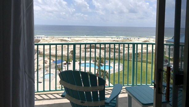 A balcony with a view of a beach, a pool, and a clear sky. - Ocean View, Beach Front Condo with Pools at Plantation Palms in Fort Morgan (Gulf Shores)