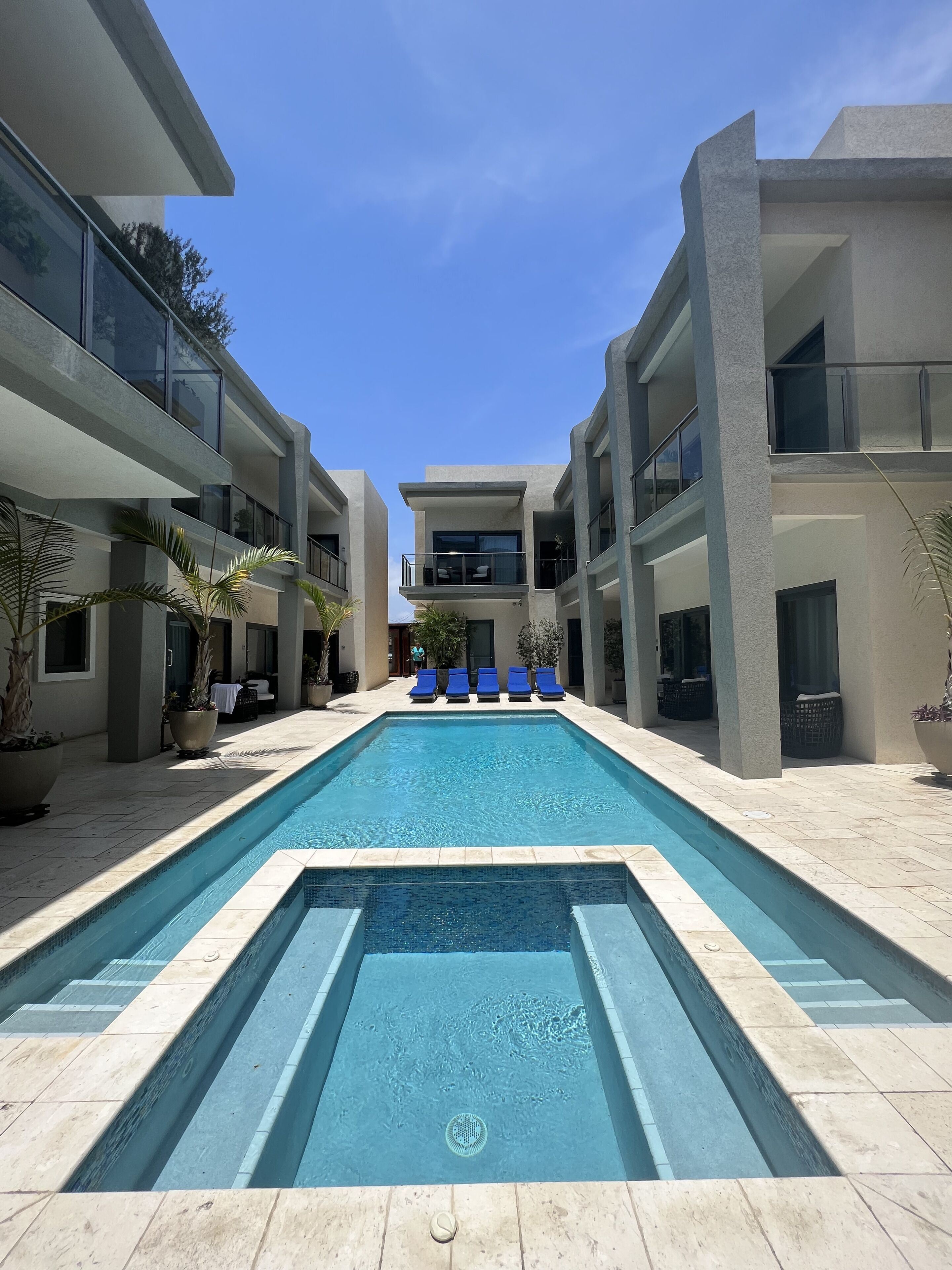 Un área de piscina moderna con piscina rectangular, sillas de descanso y plantas en macetas.