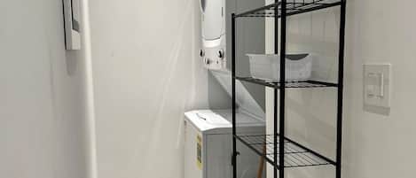A laundry room with a white washing machine, a dryer, and a metal shelving unit with a basket.