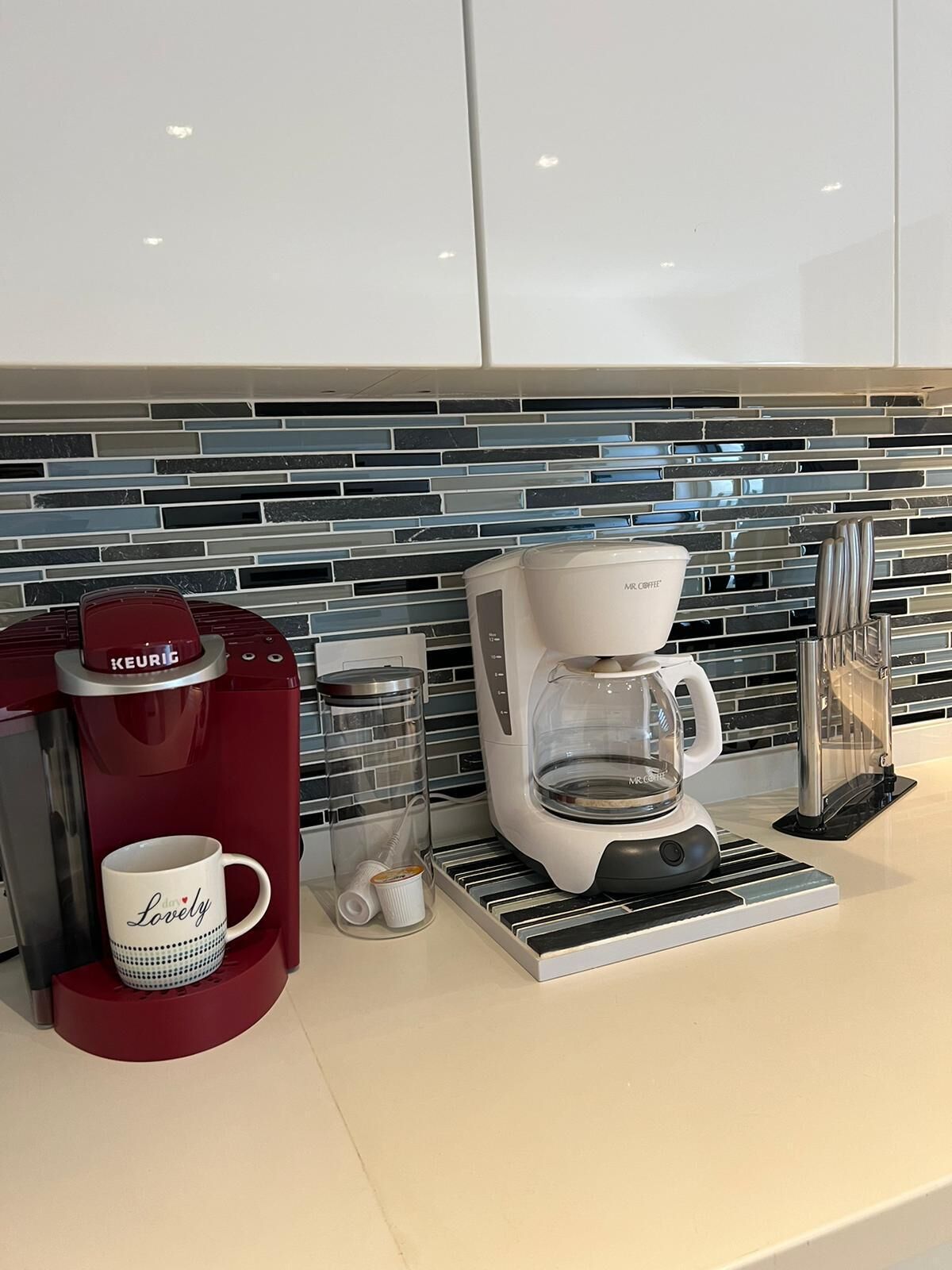 Eine Küche mit Kaffeemaschine, Tasse und einem Glasbehälter auf der Arbeitsplatte.