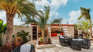Eine Außenpatio-Terrasse mit Korbmöbeln, Palmen und einem Gebäude mit Ziegeldach.