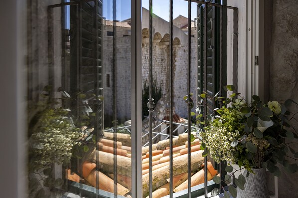 A view through a window with a metal grill, featuring terracotta steps and a brick wall in the background.