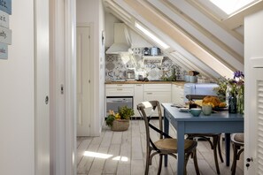 A kitchen with a sloped ceiling, white cabinets, and a dining area with a table set for two.