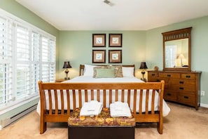 A bedroom with a wooden bed, a bench with towels, a dresser, and a mirror.