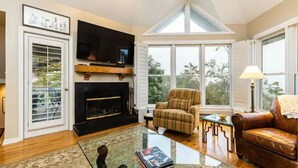 Una sala de estar con chimenea, televisor, un sillón a rayas, un sofá de cuero y una mesa de centro de vidrio.