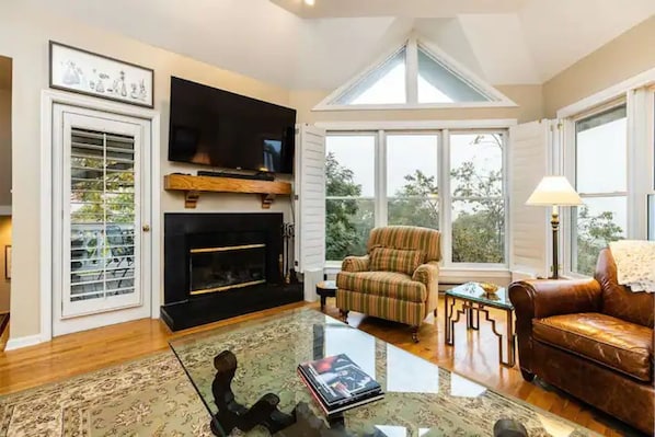 A living room with a fireplace, a television, a striped armchair, a leather sofa, and a glass coffee table.