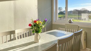 A dining table with a white tablecloth, white chairs, and a vase with flowers. - 3 bedroom accommodation in Newton Stewart (Newton Stewart)