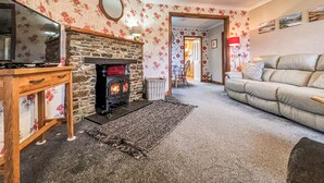 A cozy living room with a fireplace, a sofa, a television, and a dining area. - 1 bedroom accommodation in Leverburgh, Isle of Harris (Leverburgh, Isle of Harris)