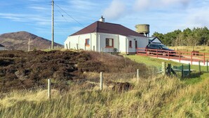 A white building with a red roof, a water tank, and a red fence in a rural setting. - 1 bedroom accommodation in Leverburgh, Isle of Harris (Leverburgh, Isle of Harris)