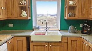 A kitchen with wooden cabinets, a white sink, a window with a view of a field, and a coffee maker. - 1 bedroom accommodation in Leverburgh, Isle of Harris (Leverburgh, Isle of Harris)