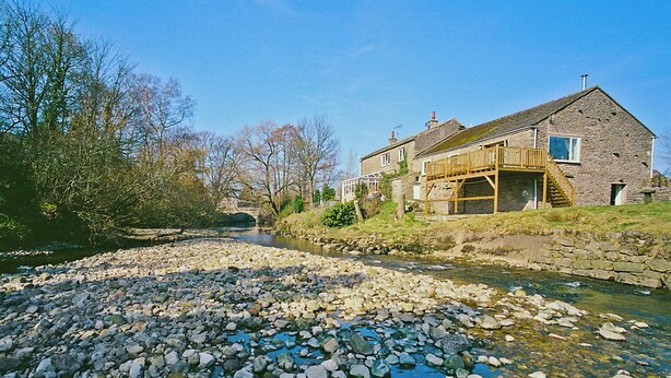 A stone house with a wooden deck and a stone bridge in the background. - 3 bedroom accommodation in Kirkby Stephen (Kirkby Stephen)