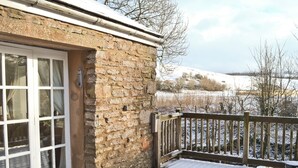 A stone building with a white door and windows, a wooden deck, and a view of a snowy landscape. - 3 bedroom accommodation in Kirkby Stephen (Kirkby Stephen)
