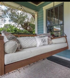A porch swing with a cushioned seat, a patterned rug, and a hanging light fixture.