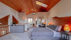 Ein geräumiges Schlafzimmer mit einem großen Bett, einer Holzbalkendecke und Blick ins angrenzende Badezimmer.