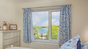 Ein Schlafzimmer mit Seeblick, einem Schminktisch mit Schubladen, einem Bett mit weißer Decke und einem Fenster mit Vorhängen.