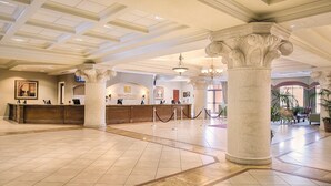 A spacious lobby with a reception desk, large columns, and a chandelier.
