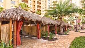 A resort with thatched-roof cabanas, palm trees, and a paved walkway.
