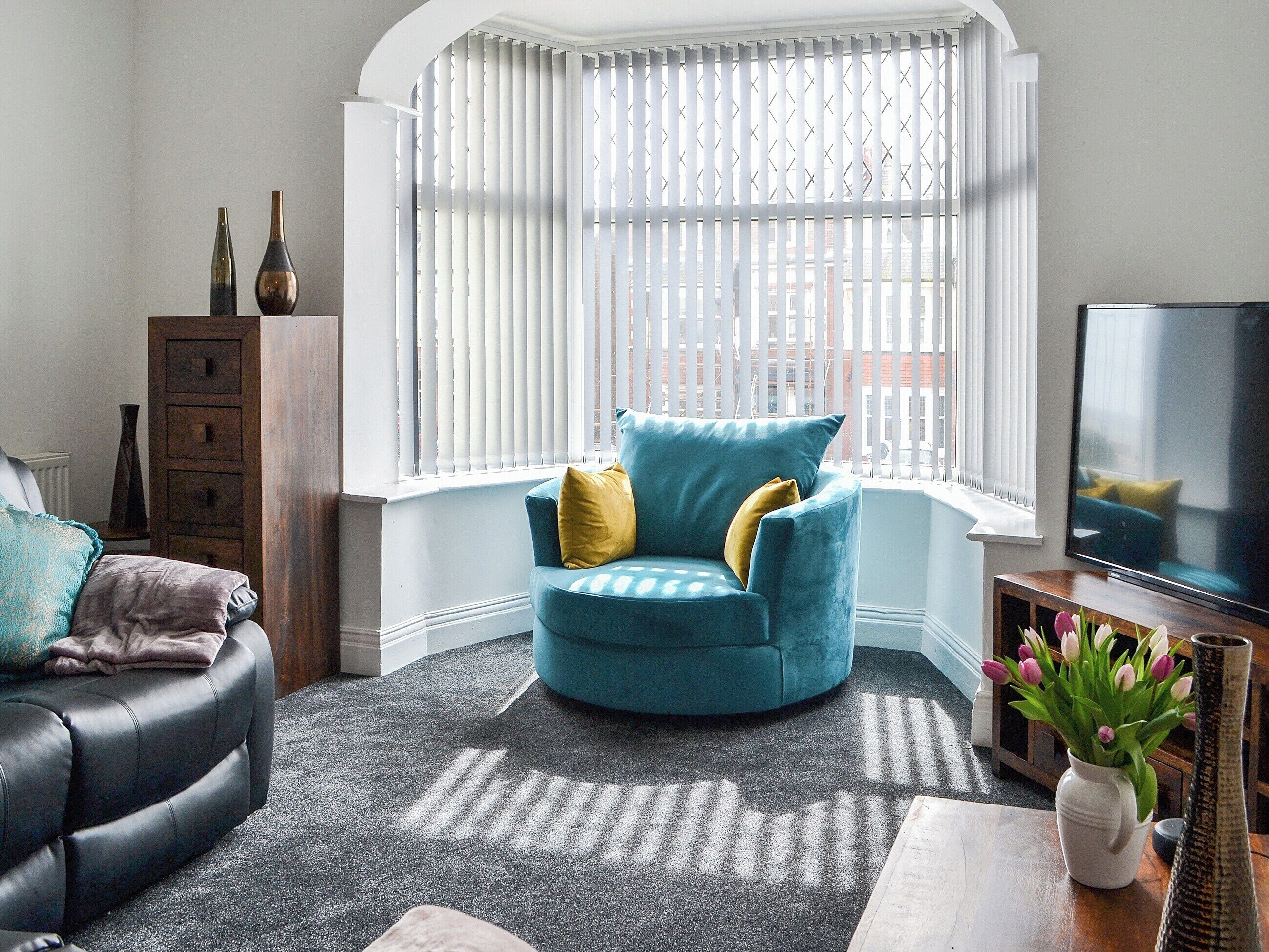 Una sala de estar con un sillón azul, un sofá negro y un armario de madera.