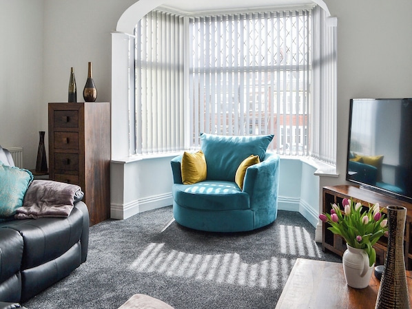 A living room with a blue armchair, a black sofa, and a wooden cabinet.