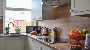 Ett modernt kök med vita skåp, en bänkskiva i trä, en diskho, en mikrovågsugn, en vattenkokare och en fruktskål.
