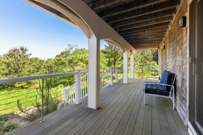 Varanda coberta com piso de madeira, guarda-corpos brancos e uma única cadeira azul.
