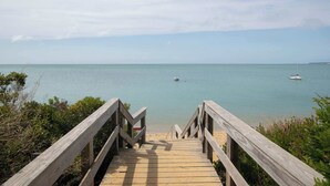 Eine Holztreppe führt zu einem Strand mit ruhigem Wasser und einem Boot in der Ferne.
