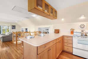 A modern kitchen with wooden cabinets, a built-in oven, and a dining area with a gray sofa and wooden chairs.