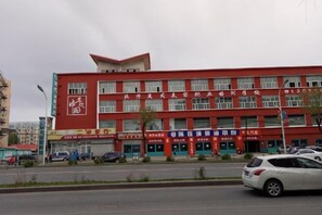 A multi-story building with a red facade, several storefronts, and a parking lot with cars. - Holiday Yizhan Express Motel (Mudanjiang)