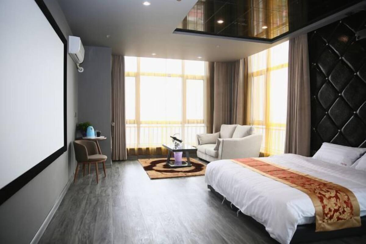 Una habitación de hotel moderna con una cama grande, una zona de estar con una mesa y vistas a la ciudad a través de amplias ventanas.