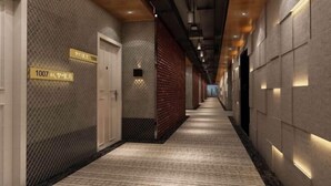 A hallway with a textured wall, a wooden ceiling, and a carpeted floor. There are doors and a sign with numbers visible.