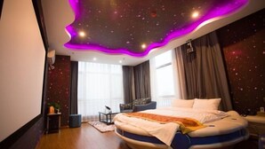 Une chambre à coucher moderne avec un lit aux lignes courbes, un plafond décoré de motifs étoilés et une vue sur l’extérieur grâce à de grandes fenêtres.