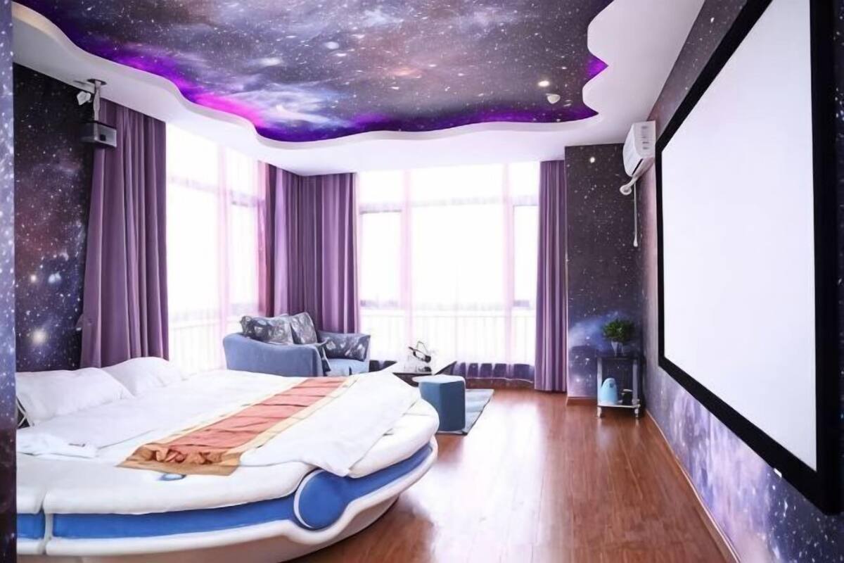 Un dormitorio con una cama, un sofá, una mesita y una pantalla de proyector.