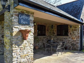 A stone building with a sign reading 'Crofter's Barn,' outdoor seating, and a dog statue.