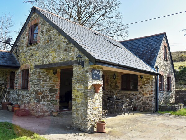 A stone building with a sign reading 'Grother's Barn,' a patio with chairs, and a stone wall.