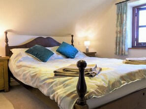 A neatly made bed with a wooden headboard, two pillows, a bedside lamp, and a window with curtains.
