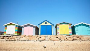 Une rangée de cabanes de plage aux couleurs vives, sous un ciel bleu azur.