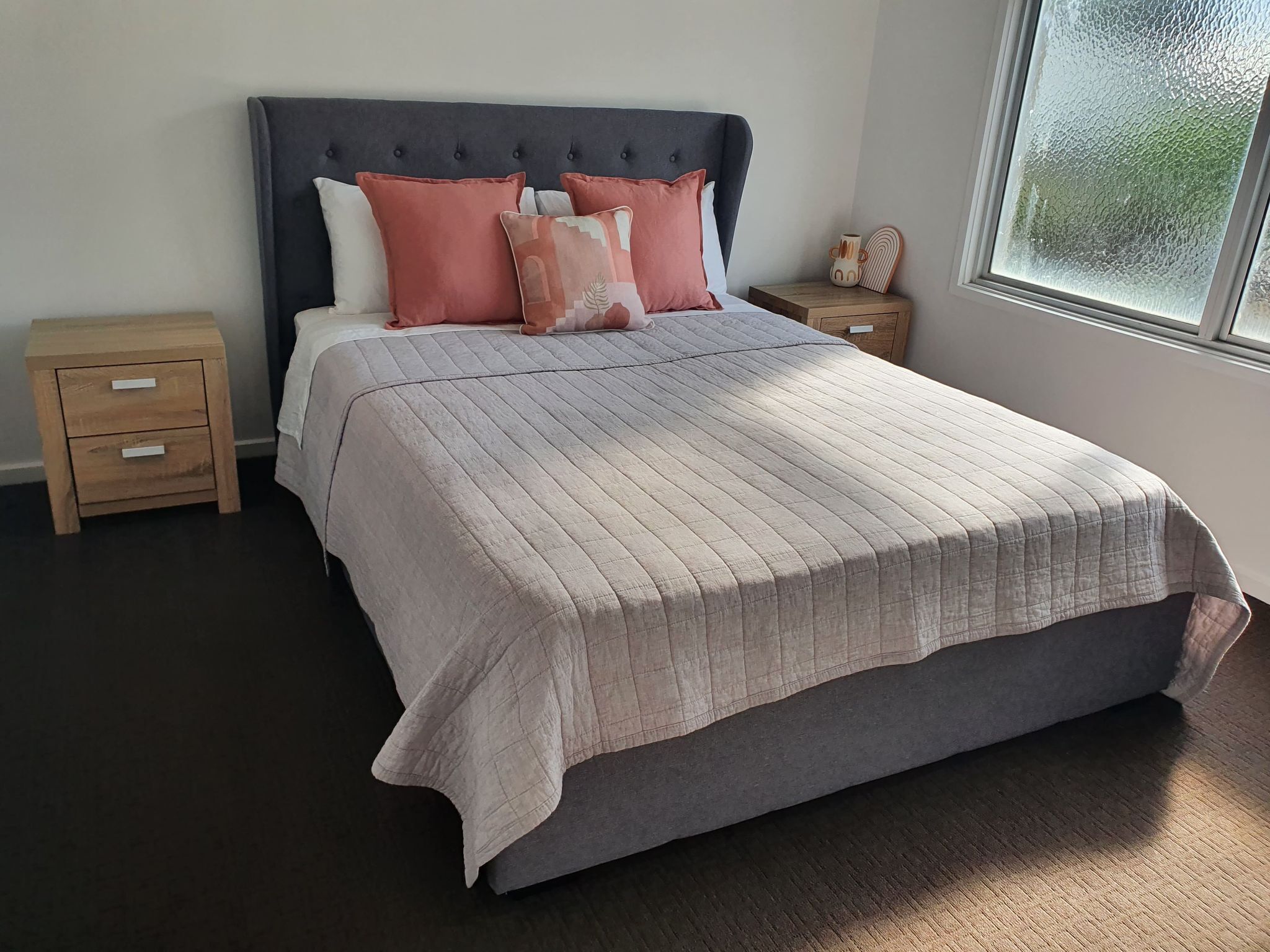 Quarto com uma cama grande, cabeceira escura e janela com vista.