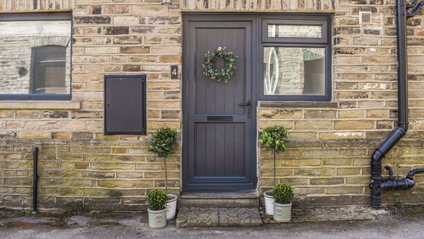 A stone building with a dark wooden door, two windows, and a small outdoor area with potted plants. - 3 bedroom accommodation in Skipton (Skipton)