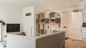A modern living room with a sofa, a TV, a white radiator, and a bookshelf filled with baskets and plants. - 3 bedroom accommodation in Skipton (Skipton)