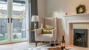 A living room with a white armchair, a fireplace, a glass door leading to a patio, and a tray with two glasses of red wine. - 3 bedroom accommodation in Skipton (Skipton)