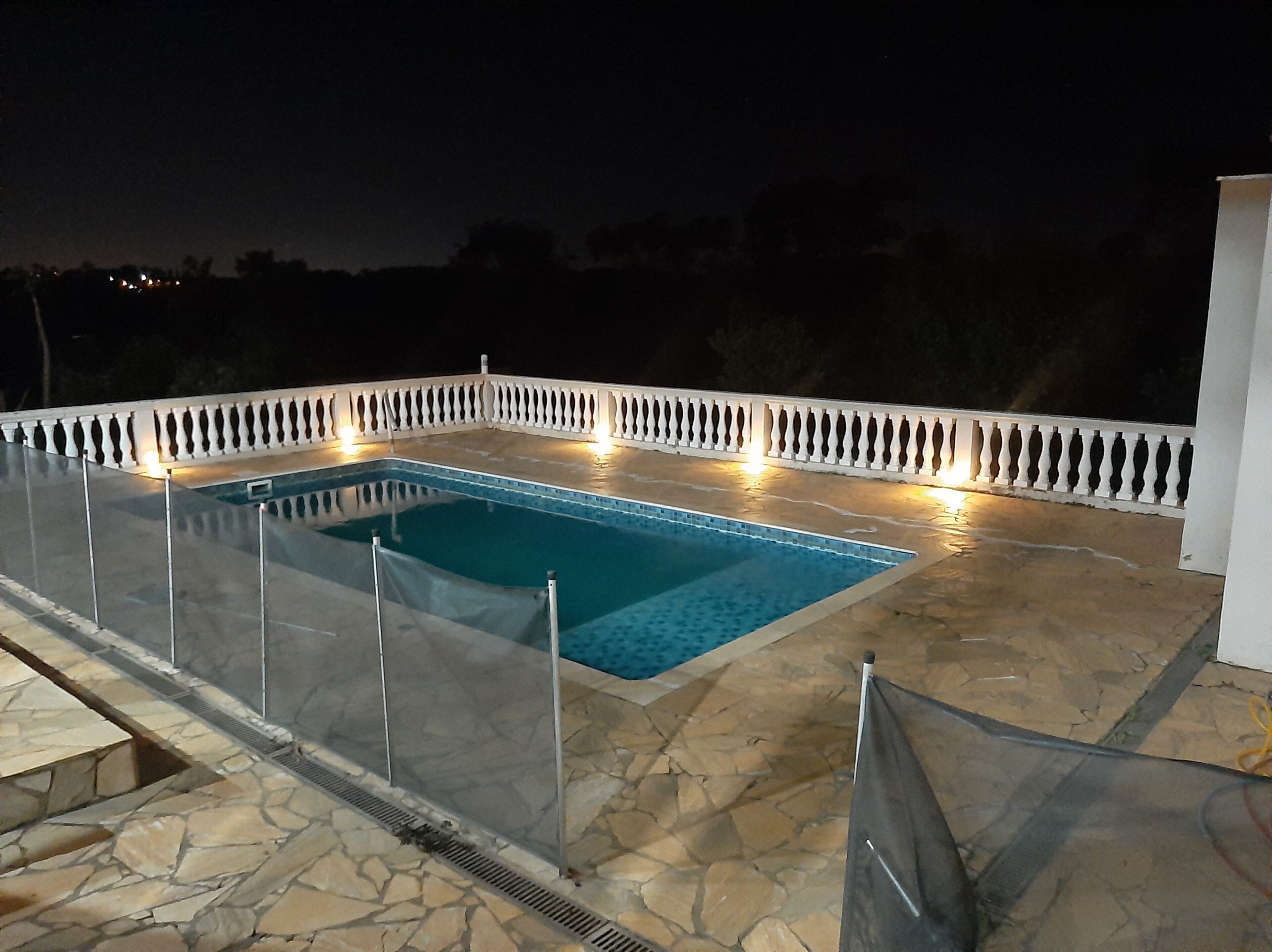 A rectangular pool with a glass enclosure, surrounded by a white balustrade, set on a stone patio.