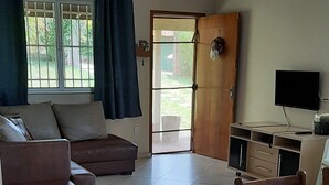 A living room with a sofa, a dining table, a TV, and a door leading outside. - Country house in Araçoiaba da Serra (Araçoiaba da Serra)