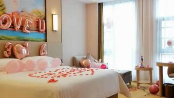 A hotel room with a large bed, a painting on the wall, and a window with curtains.