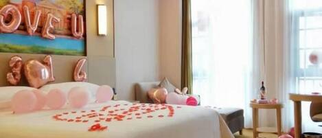 A hotel room with a large bed, a painting on the wall, and a window with curtains.