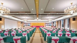 Un salón de banquetes con filas de mesas, cada una con manteles verdes y sillas decoradas con cintas rosas y blancas.