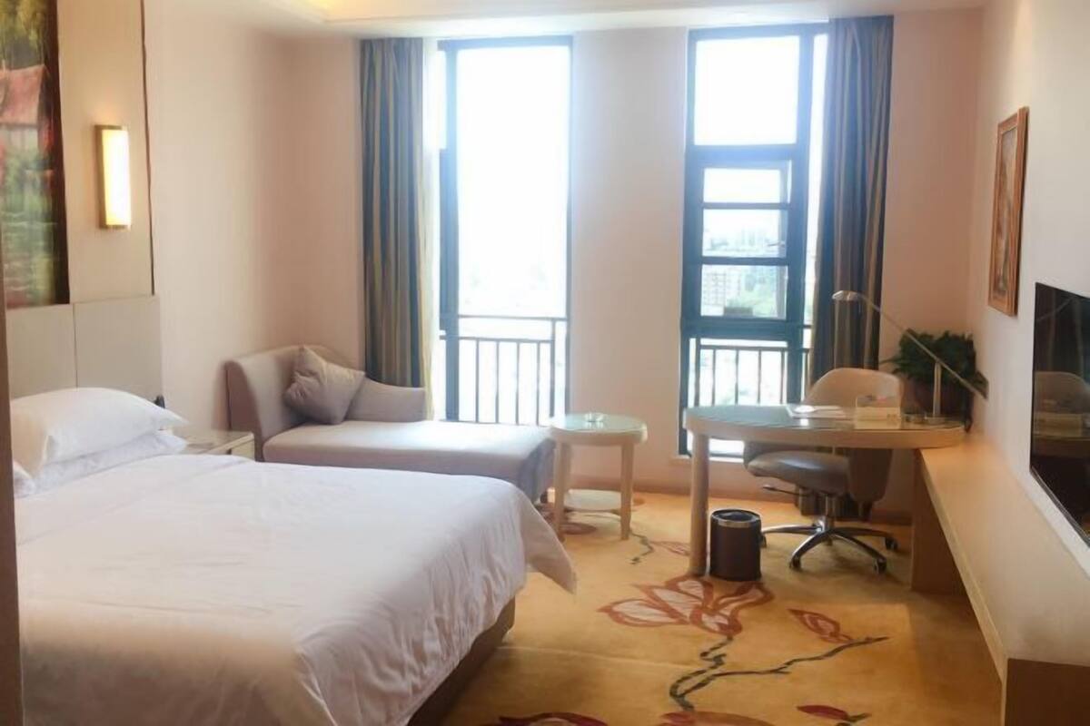 Habitación de hotel con dos camas, un escritorio, una silla, una mesita y un televisor.