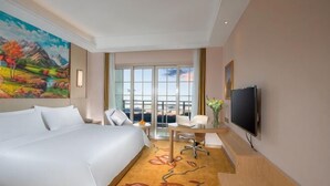 A hotel room with a large bed, a desk with a chair, a television, and a window with a view of the outdoors. - Baiyunbao International Hotel (Wangcang)